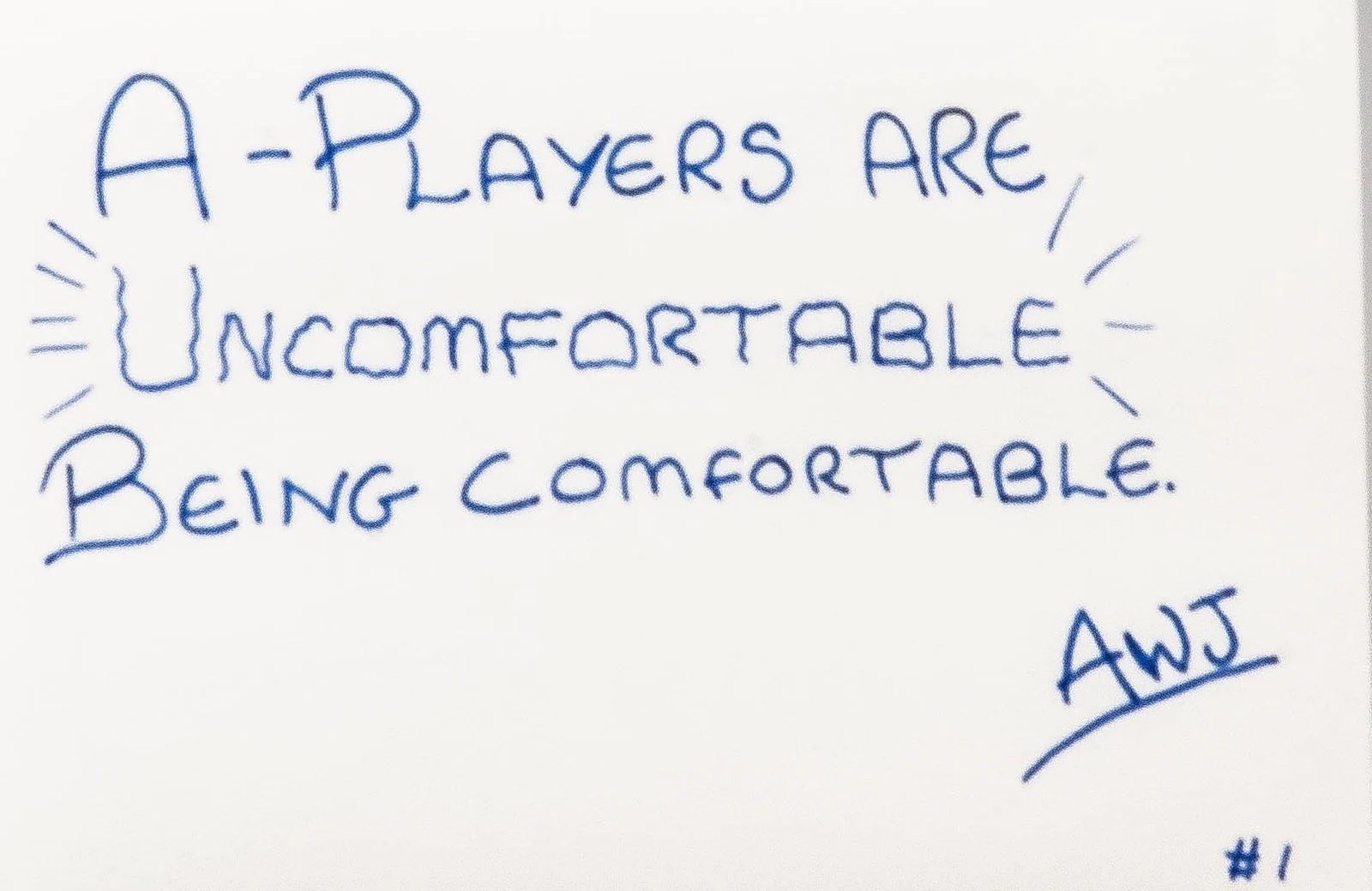 Handwritten in blue ink on a cream notebook page: A-Players are uncomfortable being comfortable. Signed AWJ, number 1.